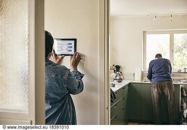 Rear view of woman using digital tablet mounted on wall at home