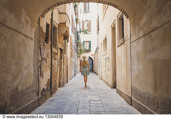 Rear view of woman walking in narrow footpath amidst buildings
