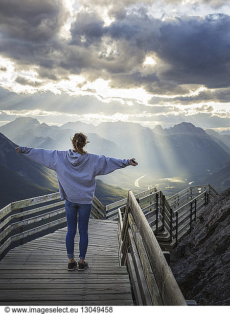 Rear view of woman with arms outstretched standing on steps against cloudy sky during sunrise, Rear view of woman with arms outstretched standing on steps against cloudy sky during sunrise