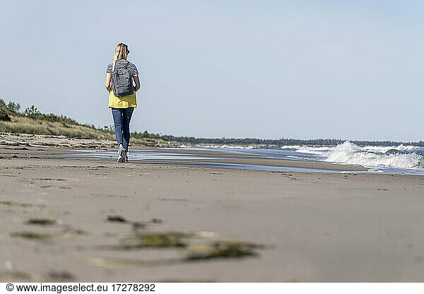 Rear view of woman with backpack walking on beach