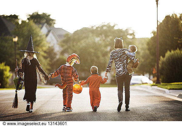 Rear view of women with children dressed for Halloween party walking on street