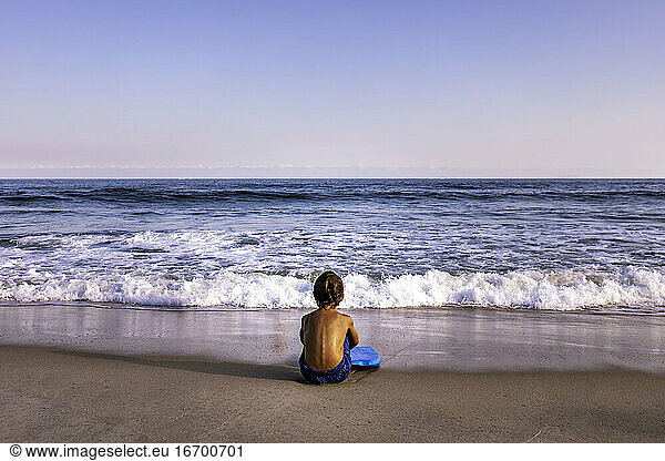 rear view of 5 years old kid sitting at the beach facing the ocean