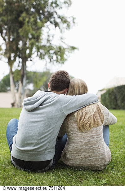 Rear view of young couple with arms around sitting at park