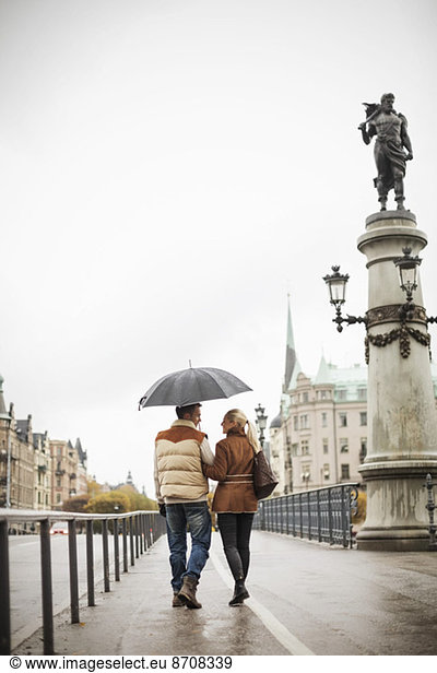 Rear view of young couple with umbrella walking on bridge