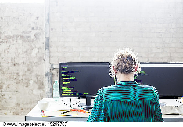 Rear view of young female computer programmer working at desk in office
