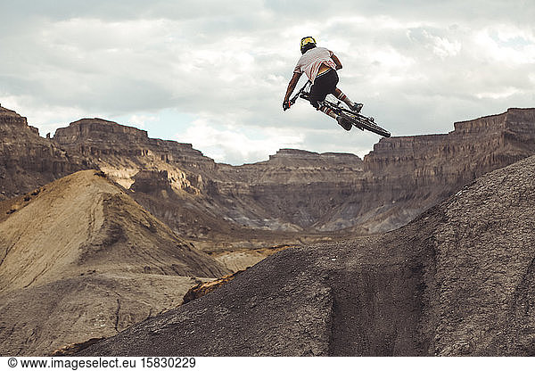 Rear view of young male jumping with mountain bike in desert landscape