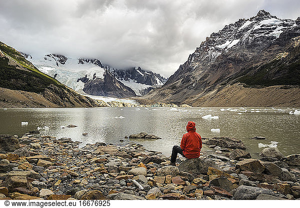 Rear view of young man in red jacket sitting by Laguna Torre  Los Glaciares National Park  El Chalten  Patagonia  Argentina