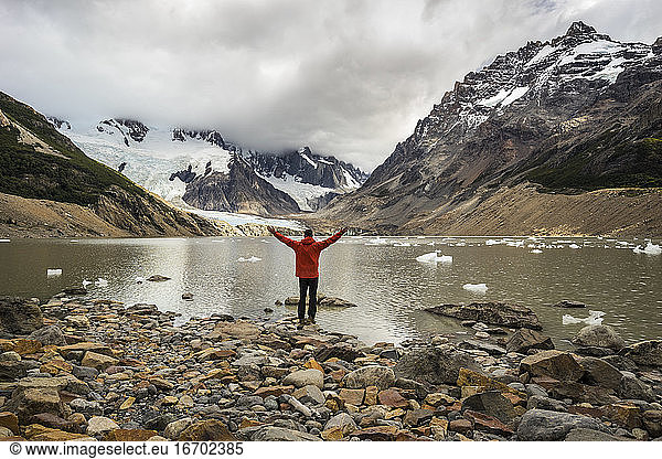 Rear view of young man in red jacket standing with open arms by Laguna Torre  Los Glaciares National Park  El Chalten  Patagonia  Argentina