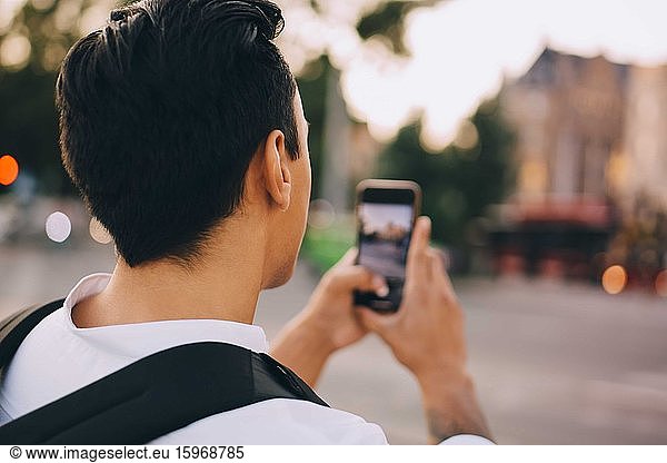 Rear view of young man photographing through smart phone in city
