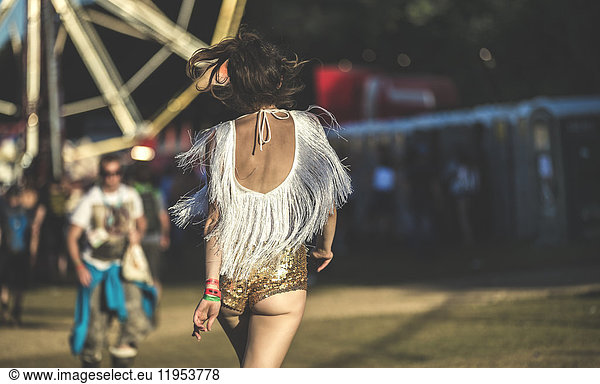 Rear view of young woman at a summer music festival wearing golden sequinned hot pants.