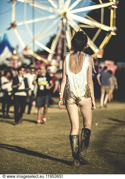 Rear view of young woman at a summer music festival wearing golden sequinned hot pants and Wellington boots.