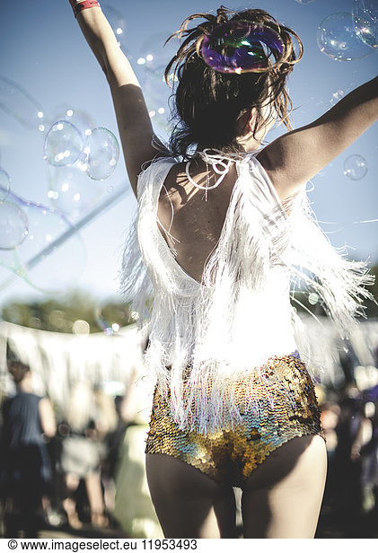 Rear view of young woman at a summer music festival wearing golden sequinned hot pants  dancing among the crowd.