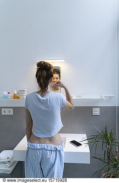 Rear view of young woman brushing teeth in bath room