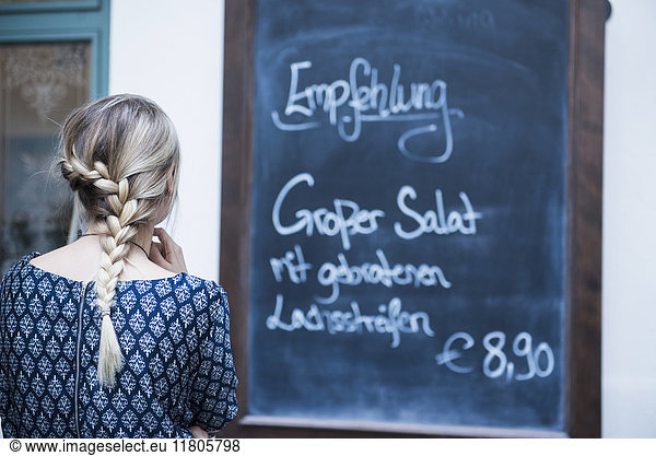 Rear view of young woman reading chalkboard menu