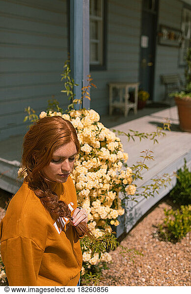 Red head woman walking past old blue porch with yellow flowers g