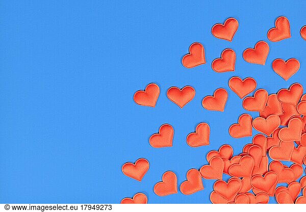 Red heart shaped confetti in corner of blue background with empty copy space