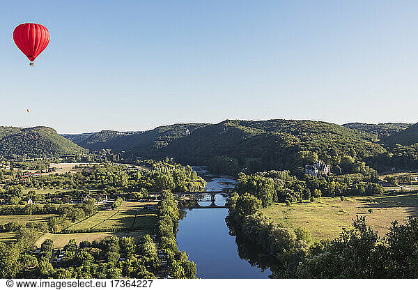 Red hot air balloon flying against clear sky over Dordogne River
