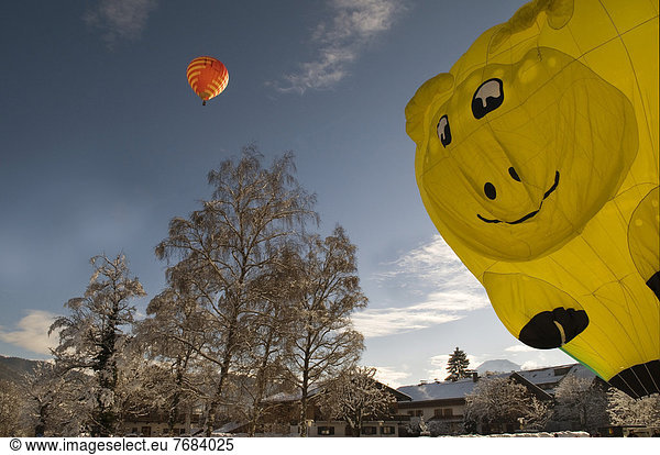 Red hot air balloon travelling against a blue sky  yellow hot air balloon in the shape of a smiling face being inflated  12th balloon festival of Tegernsee  Montgolfiade  Bad Wiessee  Tegernsee  Bavaria  Germany  Europe