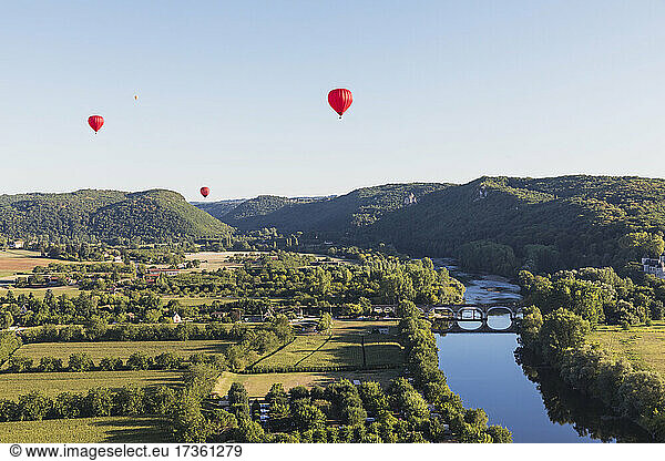 Red hot air balloons flying against clear sky over Dordogne River
