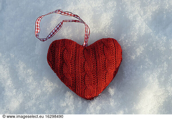 Red knitted heart lying on snow  close-up