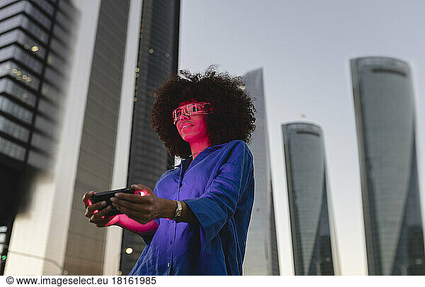 Red light falling on woman face wearing smart glasses holding smart phone in front of building