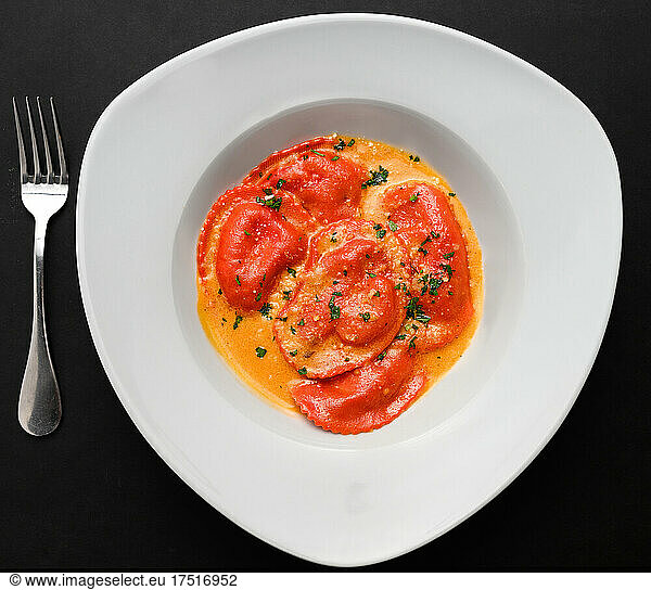 Red Ravioli in a white plate over a black background