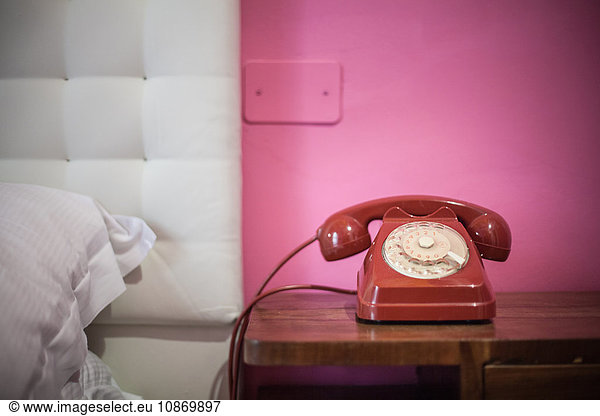 Red rotary telephone on bedside table