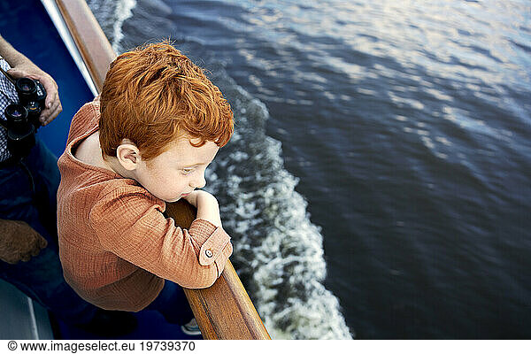 Redhead boy leaning on railing and looking at sea