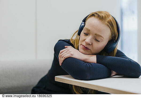 Redhead businesswoman wearing headphones and resting on desk