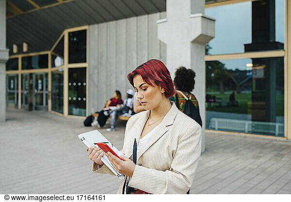 Redhead female student using smart phone in university campus
