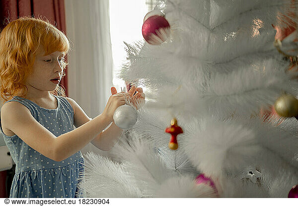 Redhead girl decorating artificial Christmas tree at home