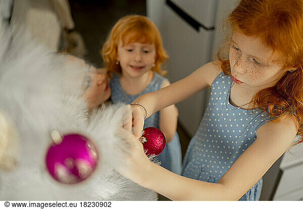 Redhead girl decorating Christmas tree by sister at home