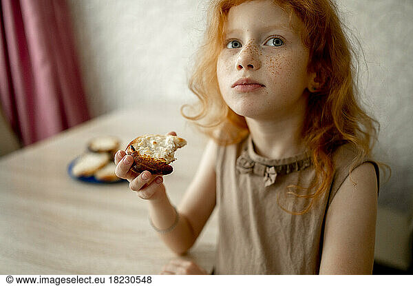 Redhead girl eating cheesecake at table
