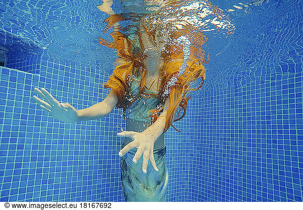 Redhead girl swimming underwater in pool