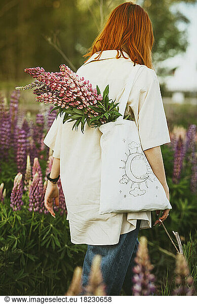 Redhead girl walking with lupin flowers in tote bag on field