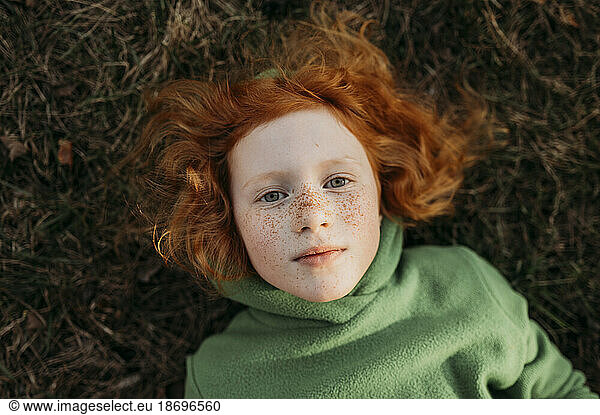 Redhead girl with freckles lying in field