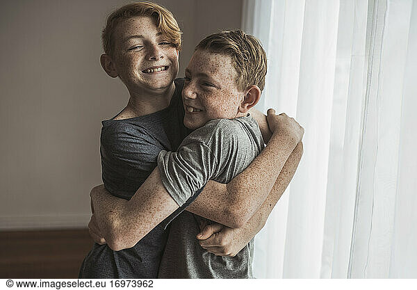 Redhead teen brothers hugging tightly in studio