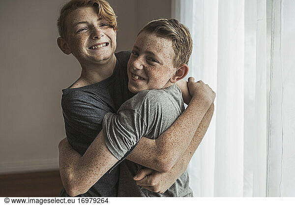 Redhead teen brothers hugging tightly in studio