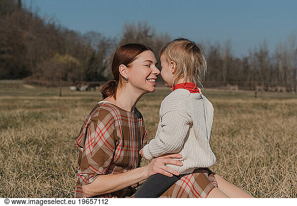 Redhead woman and her baby daughter hugging while sitting in the field