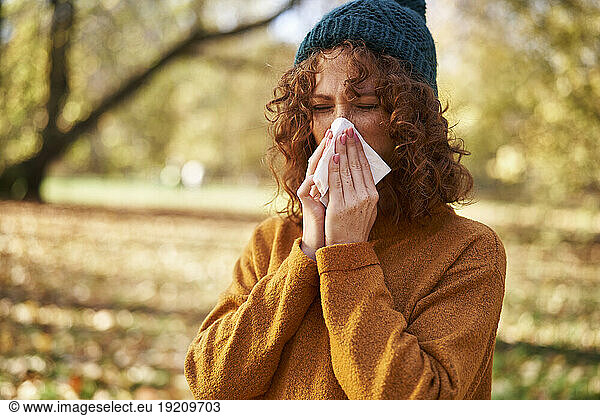 Redhead woman blowing nose with facial tissue at autumn park