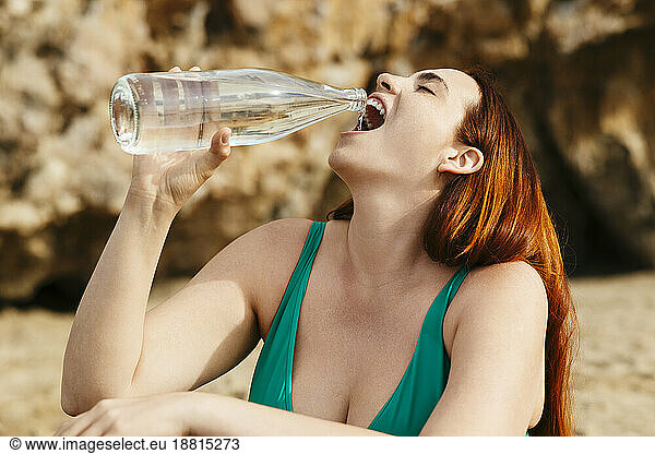 Redhead woman drinking water at beach