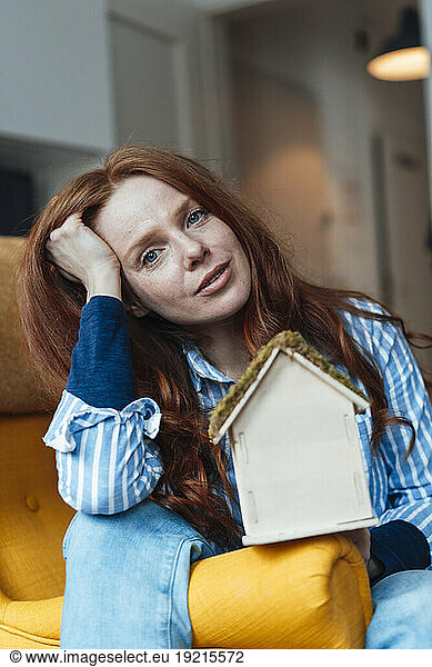 Redhead woman sitting with model house at home