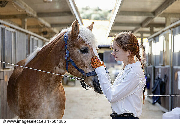 Redhead woman stroking horse at stable