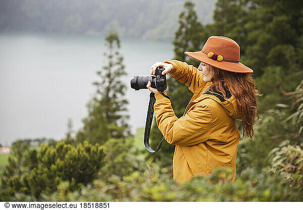 Redhead woman wearing hat photographing through camera in forest