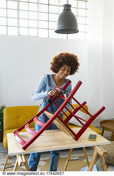 Redhead woman with electric screwdriver repairing chair at home