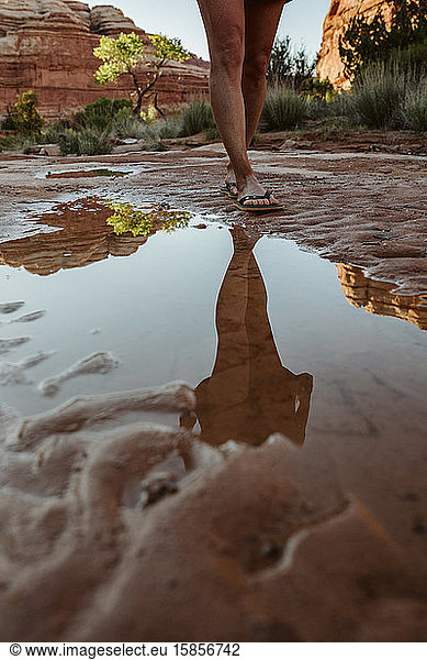 reflection in puddle of woman's legs walking in flipflops in desert mu