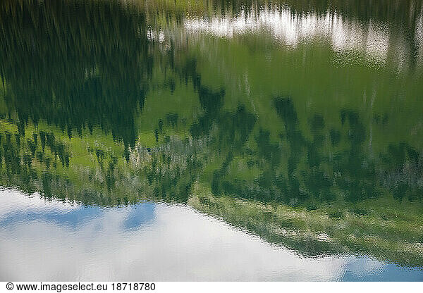 Reflection of a scenic view of alpine lake in mountains with blue sky.