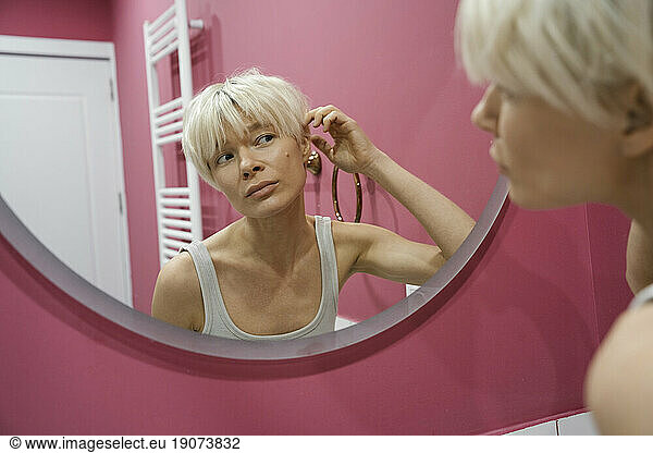 Reflection of blond woman touching hair in bathroom