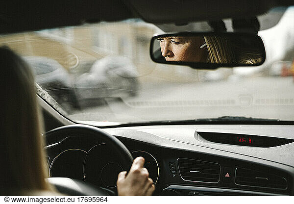 Reflection of businesswoman driving car seen on rear-view mirror