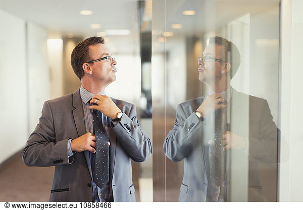 Reflection of confident businessman adjusting tie in office corridor
